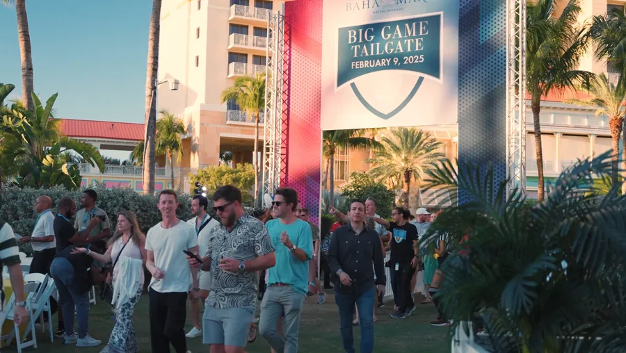 Guests arriving at the Baha Mar Big Game Tailgate event, walking past a large banner reading "Big Game Tailgate February 9, 2025" with the resort in the background.
